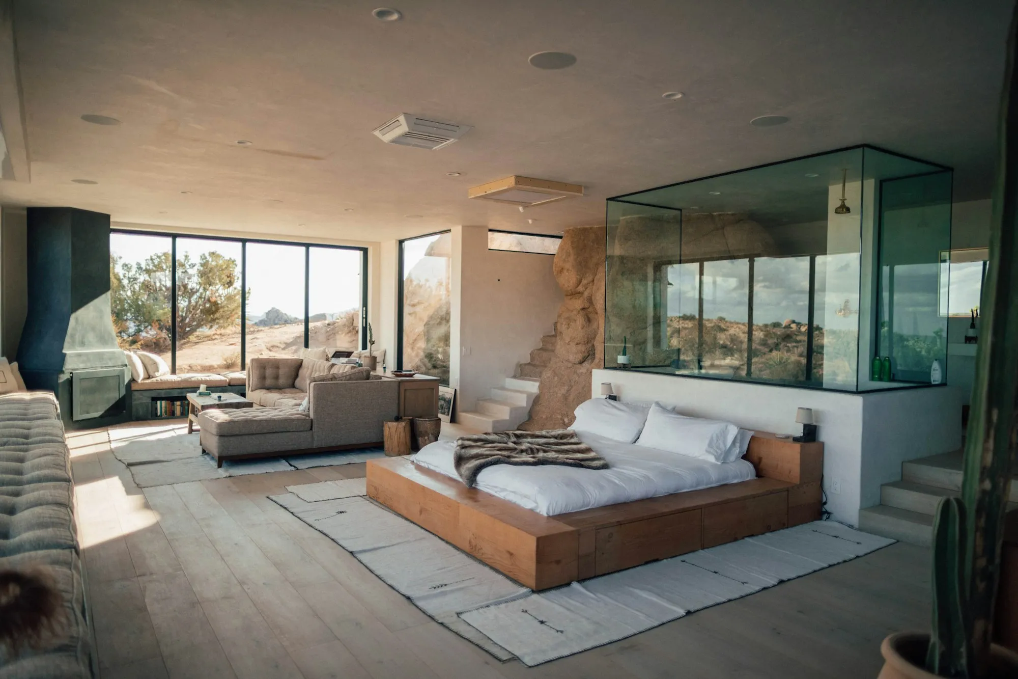 A modern bedroom with a glass wall and a view of the hills
