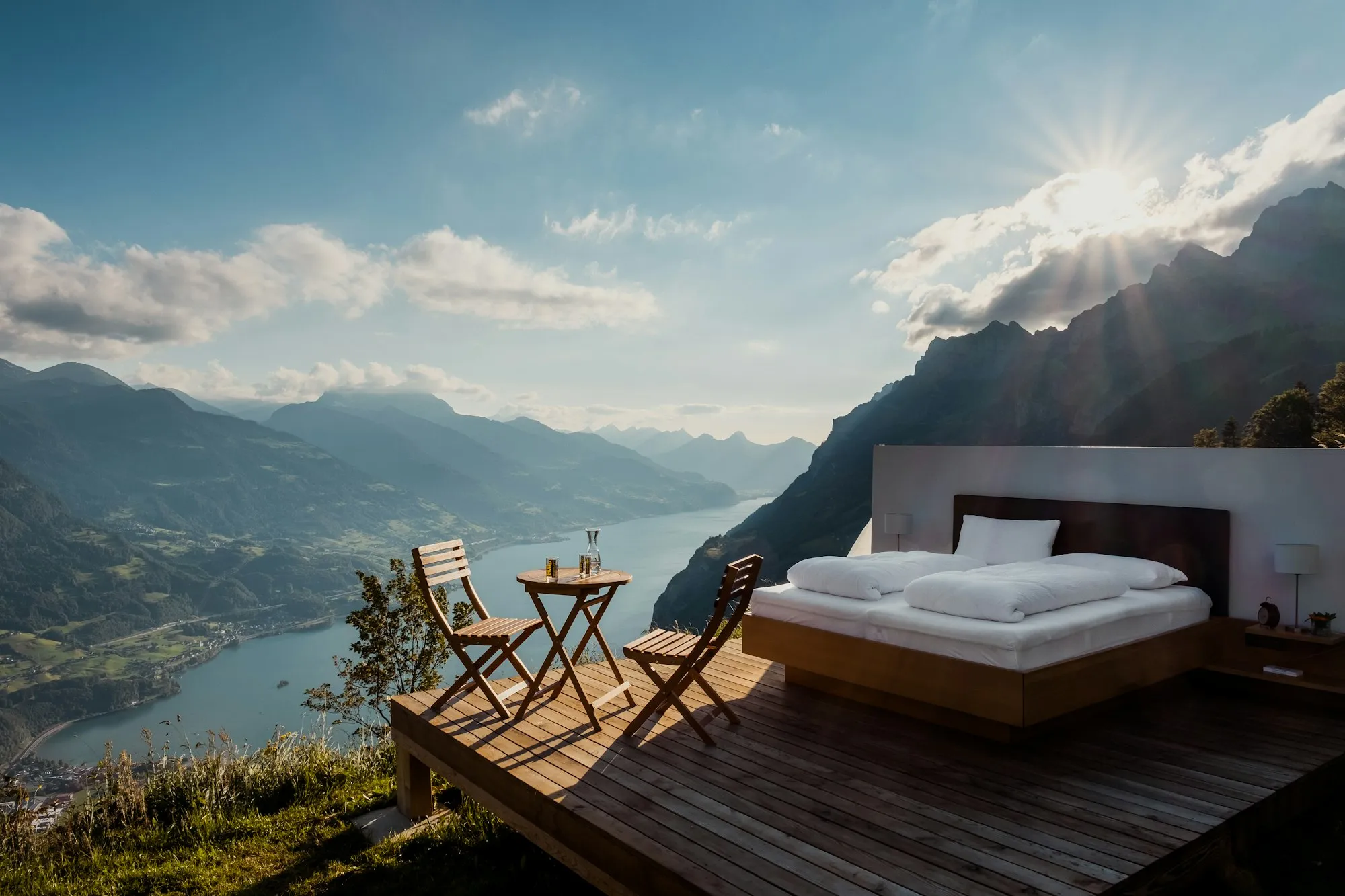 A bed on an open deck high above a lake and mountains